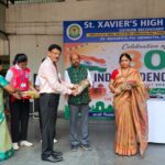 Group of students and staff on stage during independence day celebration at st Xaviers high school exchanging flower bouquets in front of a large banner